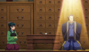 Captura de tela do anime Diários de uma Apotecária. Na imagem, os protagonistas Maomao e Jinshi estão sentados em lados opostos de uma mesa. Ela está na esquerda e ele, na direita. Ele está segurando um gato próximo ao rosto, enquanto ela o olha com uma expressão de quem o acha bobo. O título faz parte dos animes da temporada de inverno de 2025.