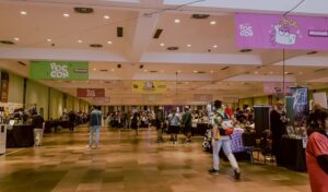 Espaço onde aconteceu o Vale dos Artistas na Poc Con 2025. Tem mesas, cadeiras e pessoas andando.